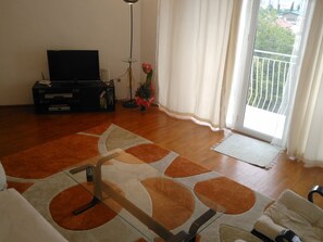 Relax in this stylish living room with a flat-screen TV, comfortable sofa, and a balcony offering views of the surrounding area.