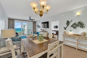 A hotel room with a dining area, a balcony with a view of the sea, and a television.