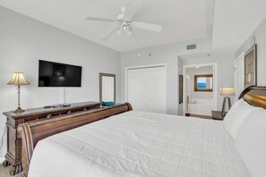 A hotel room with a bed, a television, a desk, a mirror, and a door leading to a bathroom. - Fabulous 2 BR condo! 2 Huge Pools! Fantastic Ocean Views! Great Location! (Miramar Beach)