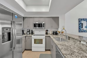 Eine moderne Küche mit Edelstahlgeräten, grauen Schränken und einer Arbeitsplatte aus Granit.