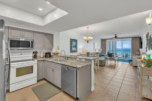 A modern kitchen with a central island, a dining area with a view, and a living room with a balcony overlooking the ocean. - Fabulous 2 BR condo! 2 Huge Pools! Fantastic Ocean Views! Great Location! (Miramar Beach)