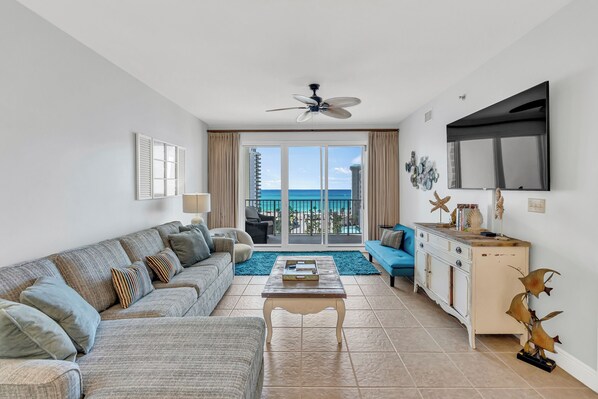 A modern living room with a sofa, coffee table, and a view of the ocean through large windows. - Fabulous 2 BR condo! 2 Huge Pools! Fantastic Ocean Views! Great Location! (Miramar Beach)