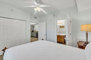 Une chambre avec un lit, un ventilateur de plafond, une salle de bain avec un lavabo et une kitchenette.