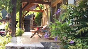 A covered outdoor seating area with stone steps, potted plants, and a wooden pergola. - Beautiful Village House (Chérizet)