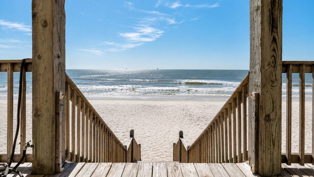 Eine Holzterrasse führt zu einem Sandstrand mit Blick auf den Ozean.