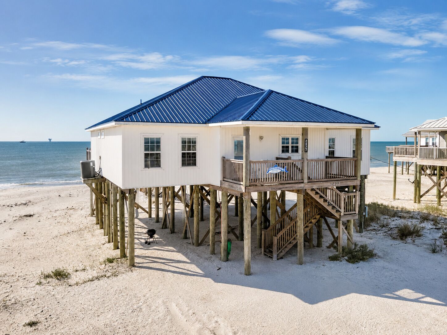 Une maison de plage avec un toit bleu, une terrasse en bois et de nombreuses fenêtres.
