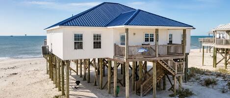 Une maison de plage avec un toit bleu, une terrasse en bois et de nombreuses fenêtres.