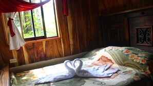 A wooden room with a bed featuring a floral bedspread and a swan-shaped towel. - Monteverde romantic cabaña (Monteverde)