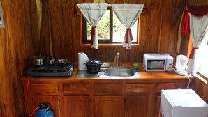 A compact kitchen with wooden cabinets, a gas stove, a microwave, a coffee maker, and a sink. - Monteverde romantic cabaña (Monteverde)