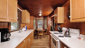 A kitchen with wooden cabinets, a stove, a kettle, and a dining table with chairs. - Charming Gatlinburg cottage walking distance to Gatlinburg downtown! (Gatlinburg)