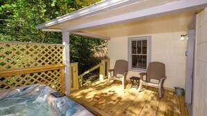 A wooden deck with a hot tub, two chairs, and a window. - Charming Gatlinburg cottage walking distance to Gatlinburg downtown! (Gatlinburg)