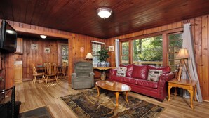 A wooden interior with a red leather sofa, a wooden coffee table, and a television on a wooden stand. - Charming Gatlinburg cottage walking distance to Gatlinburg downtown! (Gatlinburg)