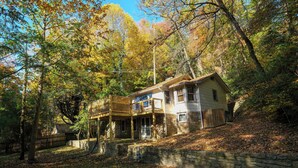 A two-story house with a balcony, surrounded by trees and a stone wall. - Charming Gatlinburg cottage walking distance to Gatlinburg downtown! (Gatlinburg)