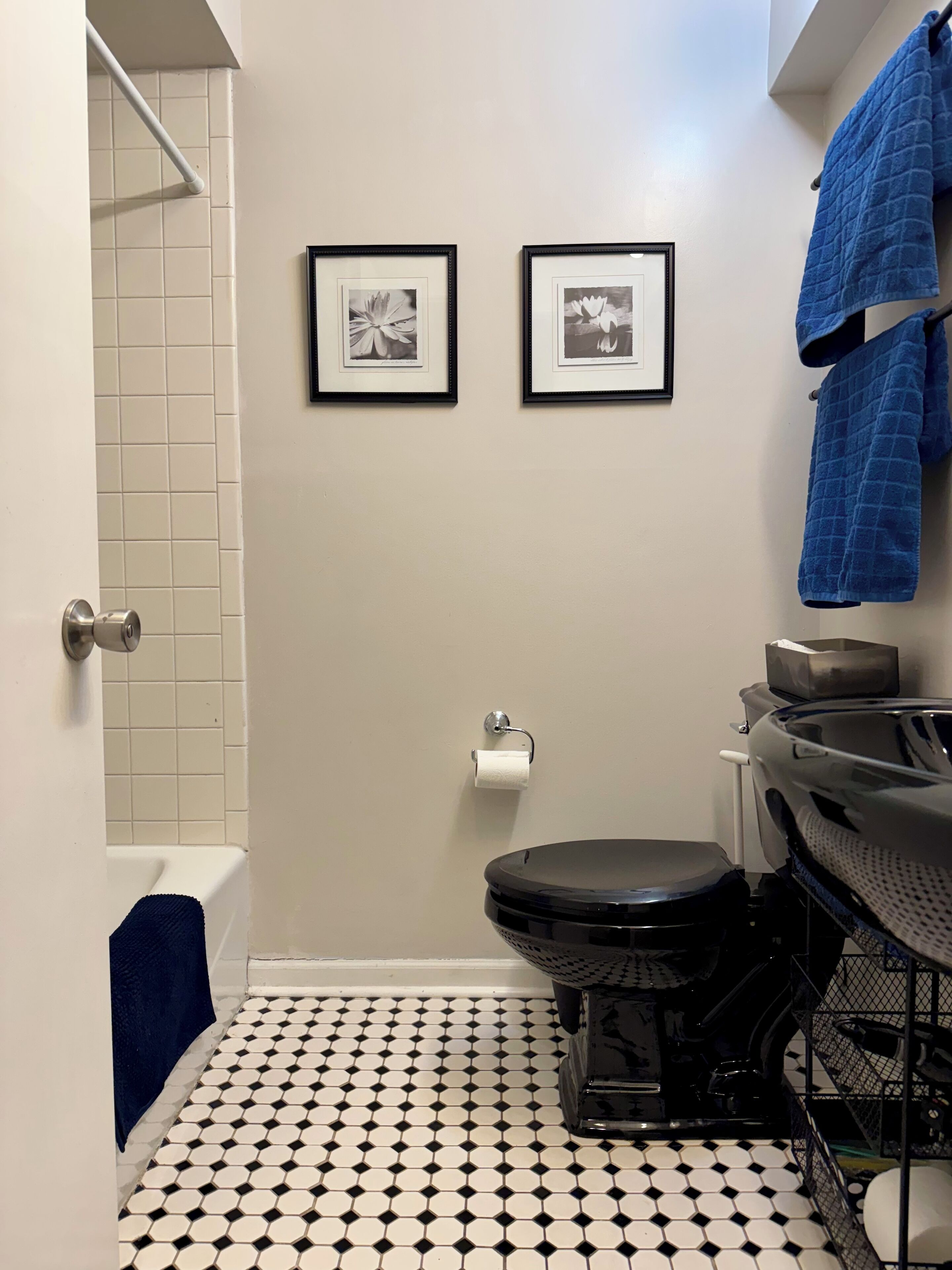 Un baño con suelo de baldosas blanco y negro, un inodoro, un lavabo y dos cuadros en la pared.