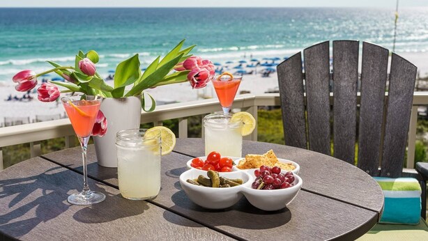 A table with drinks, a plant, and snacks by a beach. - BREATHTAKING WATER VIEWS!!! Pools/Hot TubRestaurant/Pickleball/PutPutGolf - Tops'l Beach Manor (Miramar Beach)