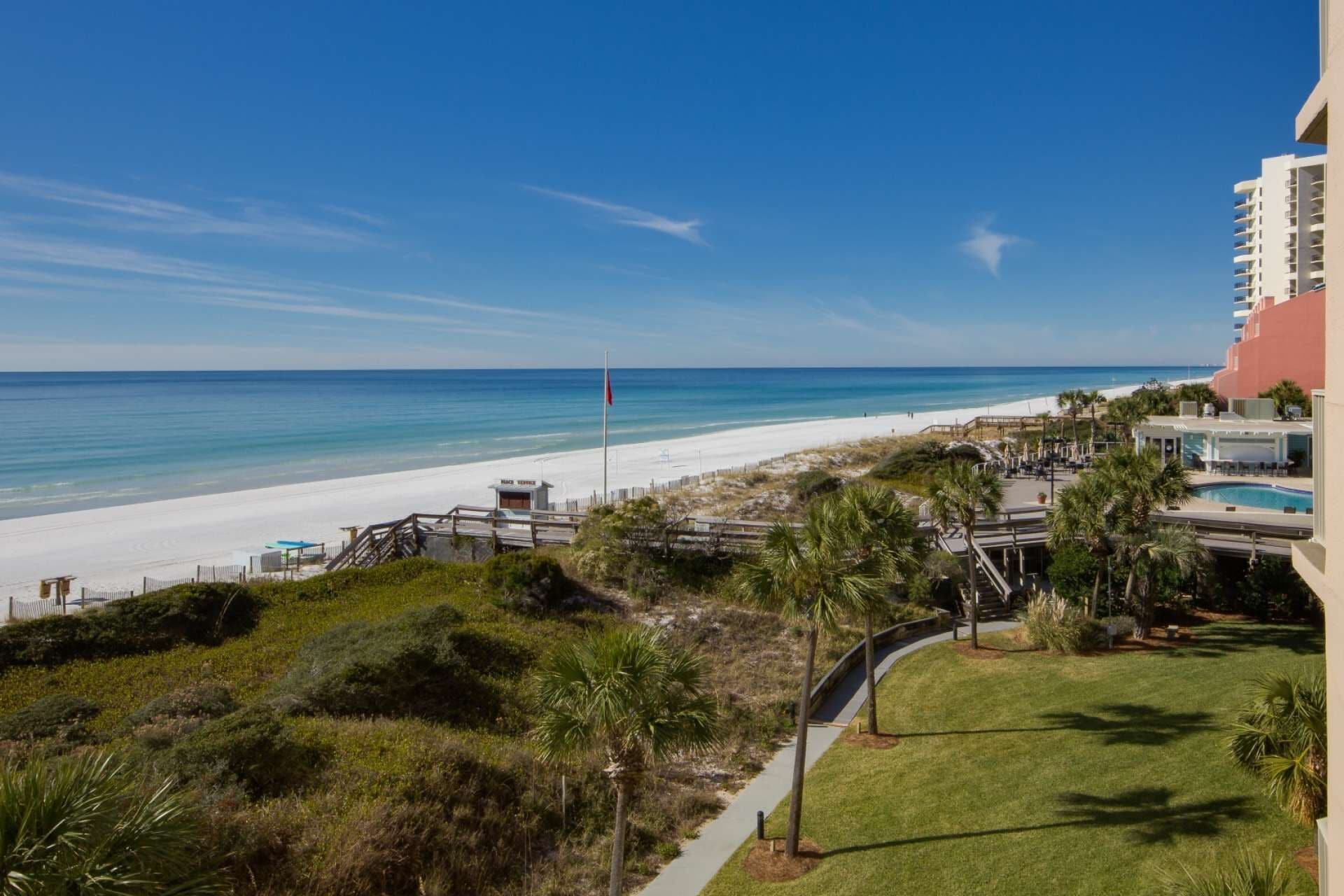 A beach view with a lifeguard tower, a pool area, and a building with balconies overlooking the ocean.