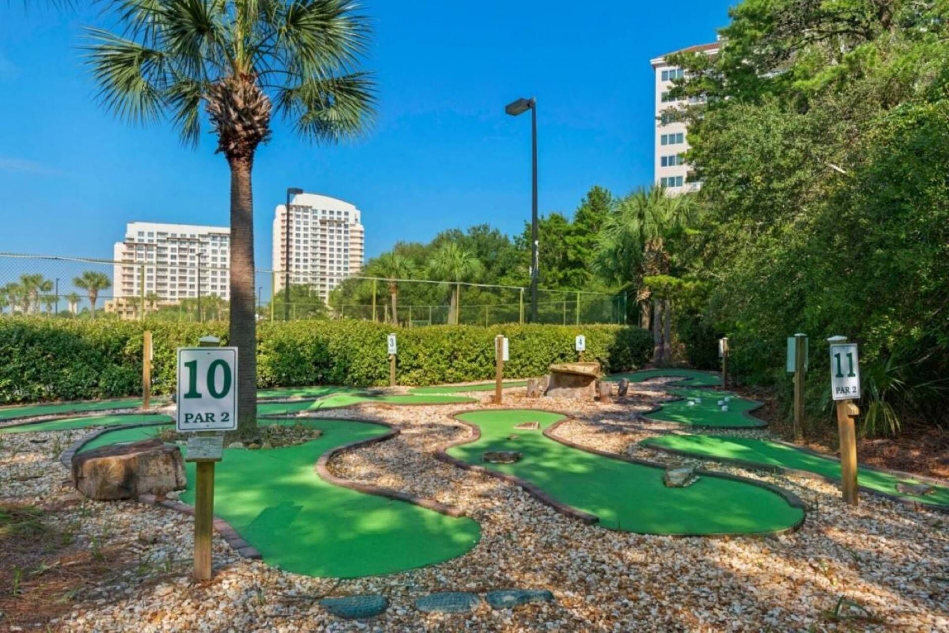Ein Minigolfplatz mit nummerierten Bahnen, umgeben von Grünflächen und Palmen.