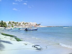 Una playa con barcos, un edificio blanco con arcos y un cielo despejado.