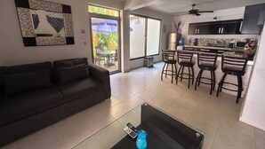 Una sala de estar con sofá, una mesa de centro y una cocina con barra y taburetes.