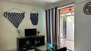 Una sala de estar moderna con una mesa de centro de vidrio, un televisor de pantalla plana sobre un mueble negro y un ventanal corredizo que da a un espacio exterior.