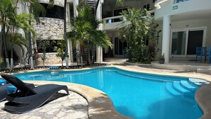 Piscina con sillas de descanso, rodeada de palmeras y un muro de piedra.