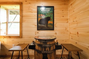 A wooden cabin interior with a poster of Great Smoky Mountains National Park, a wooden barrel, and two small tables.