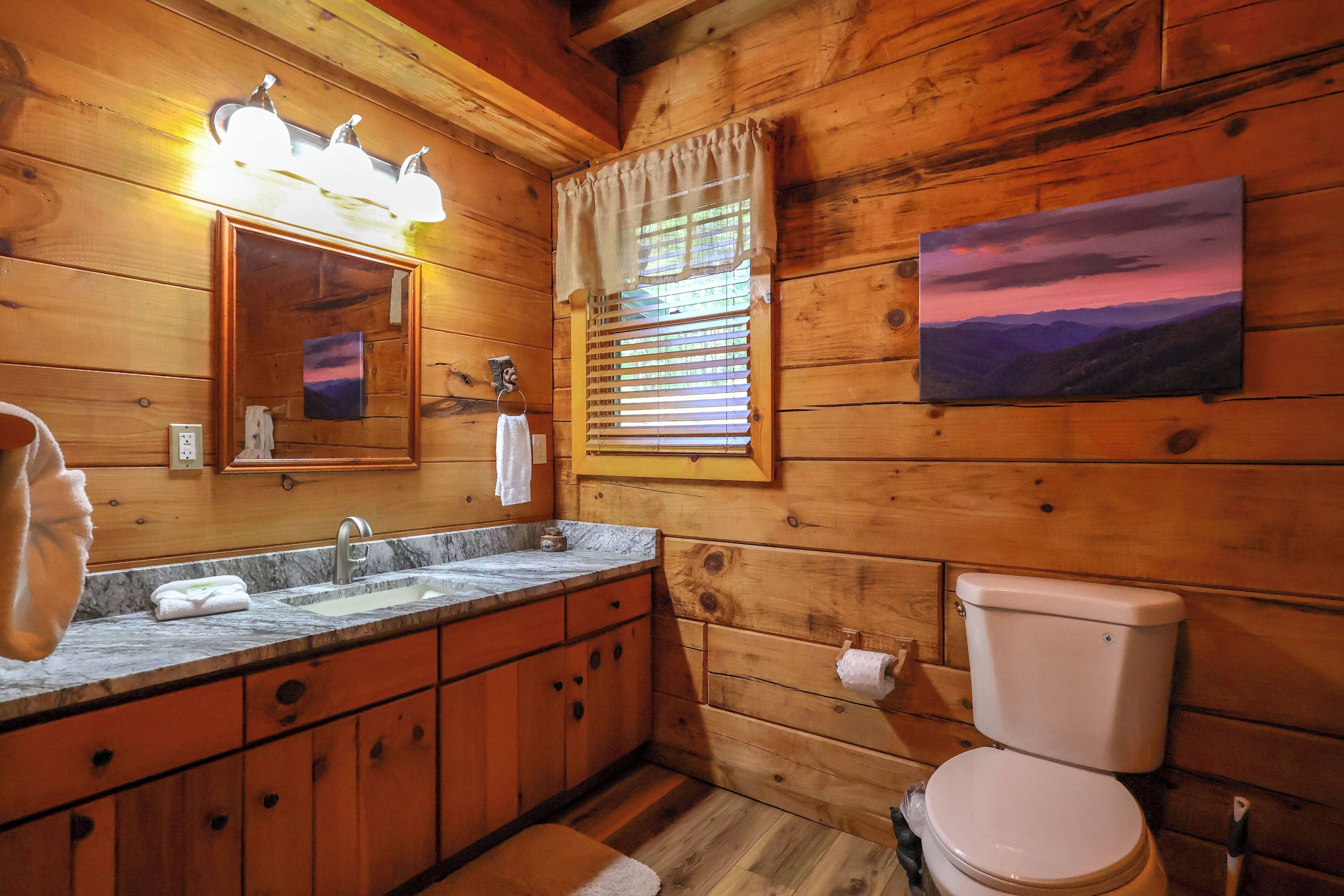 A wooden cabin bathroom with a sink, mirror, toilet, and a painting on the wall.