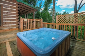 A wooden cabin with a hot tub on a deck.