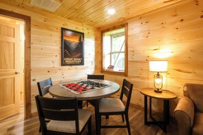 A wooden interior with a round table, chairs, a chessboard, a lamp, and a poster of the Great Smoky Mountains.