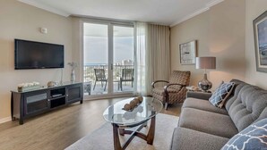 Un salon équipé d’un téléviseur à écran plat, d’une table basse en verre, d’un canapé, d’un fauteuil et d’un balcon avec vue.