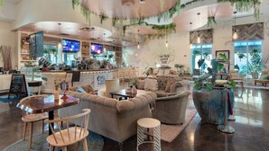 Un café chaleureux avec un coin bar, des sièges confortables et des plantes suspendues.