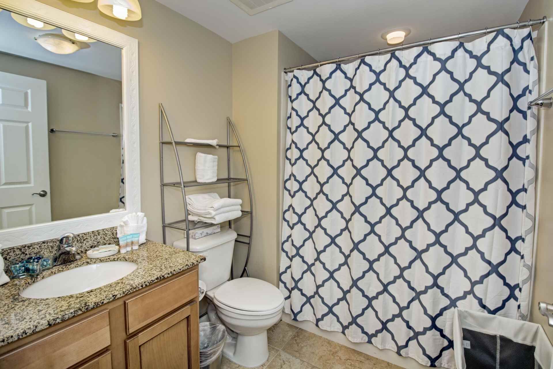 A bathroom with a granite countertop sink, a white toilet, a towel rack, and a shower curtain with a geometric pattern.