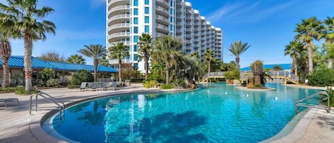A hotel with a large pool surrounded by palm trees and a clear blue sky.