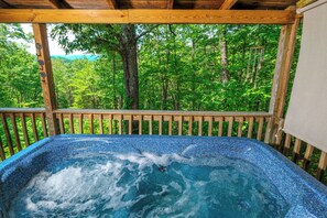 A hot tub with a wooden deck and a view of a forest. - Cute, classic, comfy log cabin with mountain views, amazing stone fireplace, and a hot tub! (Sevierville)
