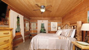 Ein Schlafzimmer einer Holzhütte mit einem Bett, einem Deckenventilator, einem Schminktisch und einem Fernseher an der Wand.