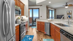 Una cocina moderna con armarios de madera, electrodomésticos de acero inoxidable y un amplio ventanal con vistas al océano.