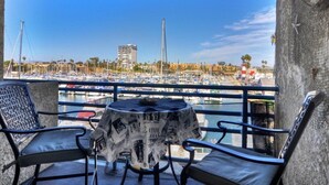 Un balcón con dos sillas y una mesa, con vista a un puerto deportivo con barcos y edificios.