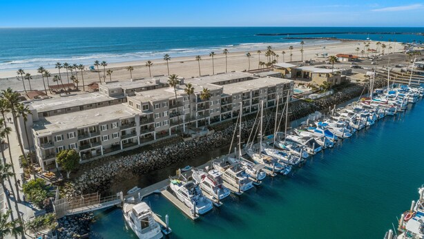 Un puerto deportivo con barcos amarrados, una playa con palmeras y un complejo de edificios de varios pisos.