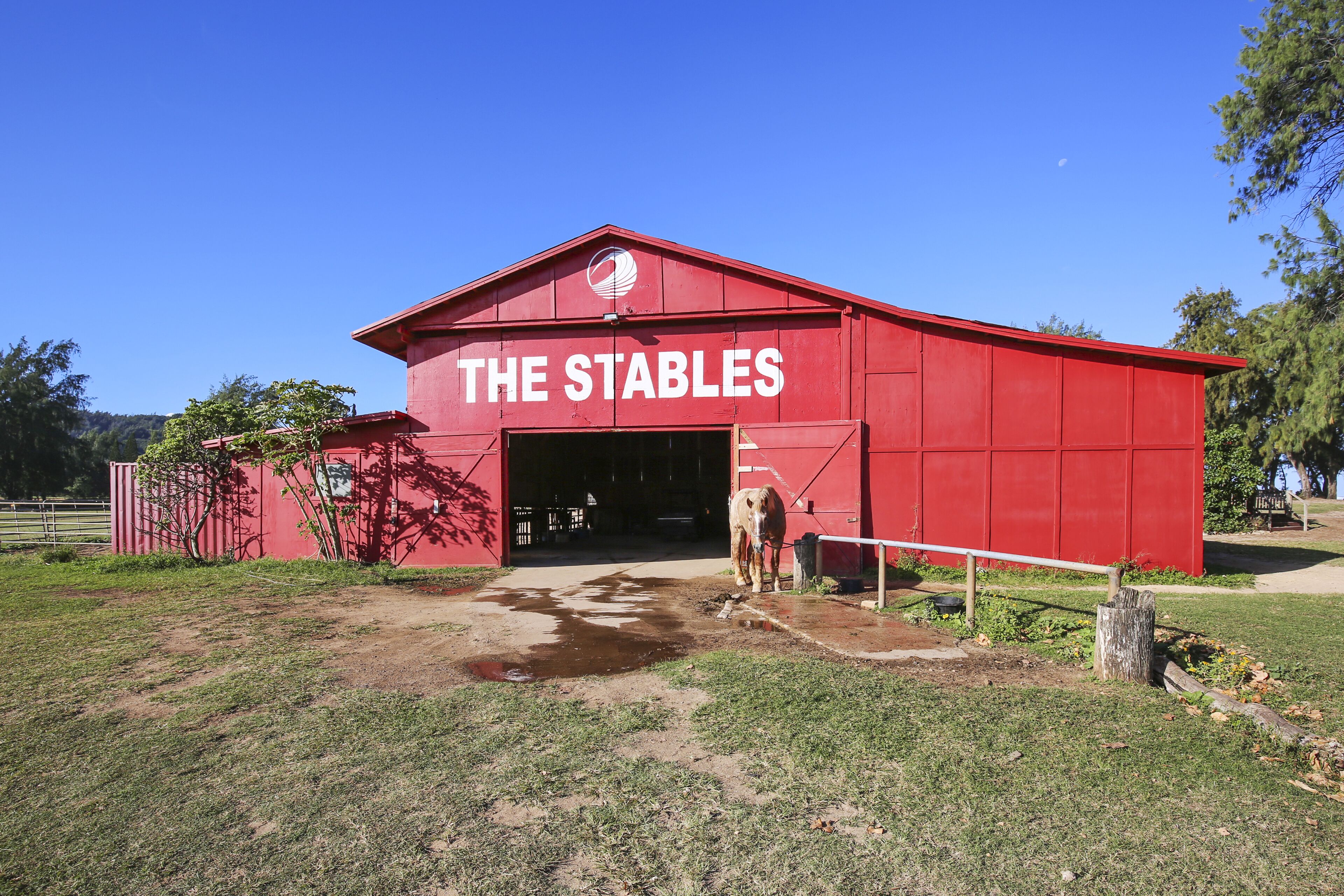 A red barn with the sign "THE STABLES" and a horse standing in front.
