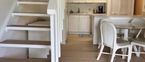 Una escalera conduce a una cocina con armarios blancos y un comedor con una mesa y sillas.