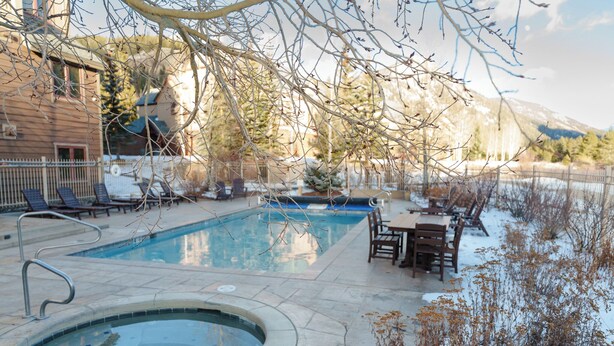 Une piscine avec un jacuzzi, entourée d’un espace de détente extérieur et offrant une vue sur les montagnes.