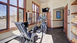 Une salle de sport à domicile équipée de matériel d’exercice, dotée de grandes fenêtres et d’un téléviseur.