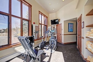 Un gimnasio en casa con equipo de ejercicio, ventanas amplias y un televisor.