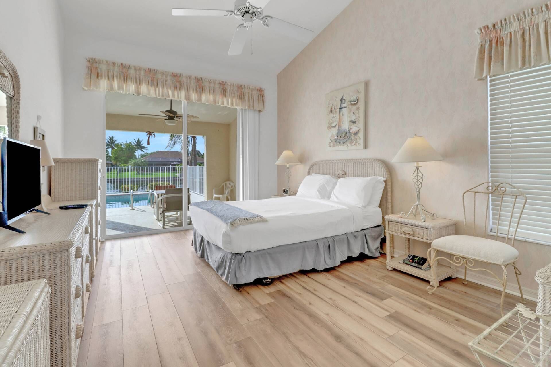 Un dormitorio con cama, televisión, escritorio y balcón con vista a una piscina.