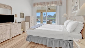 Ein Schlafzimmer mit Bett, Fernseher, Kommode und Blick auf einen Swimmingpool.