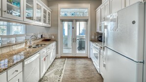 A kitchen with white cabinets, granite countertops, a stainless steel sink, and a refrigerator. - Aquaholic*CoolVibes*BeachSvc*BeachGear*PoolAccess (Miramar Beach)