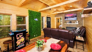 Un interior acogedor con vigas de madera, una pared verde, una mesa de juegos y una zona de estar con televisor.