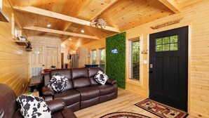 Interior acogedor de una cabaña de madera con un sofá de cuero, una puerta negra y una pared verde.