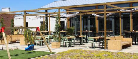 An outdoor seating area with tables and chairs, a swing set, and a covered patio.