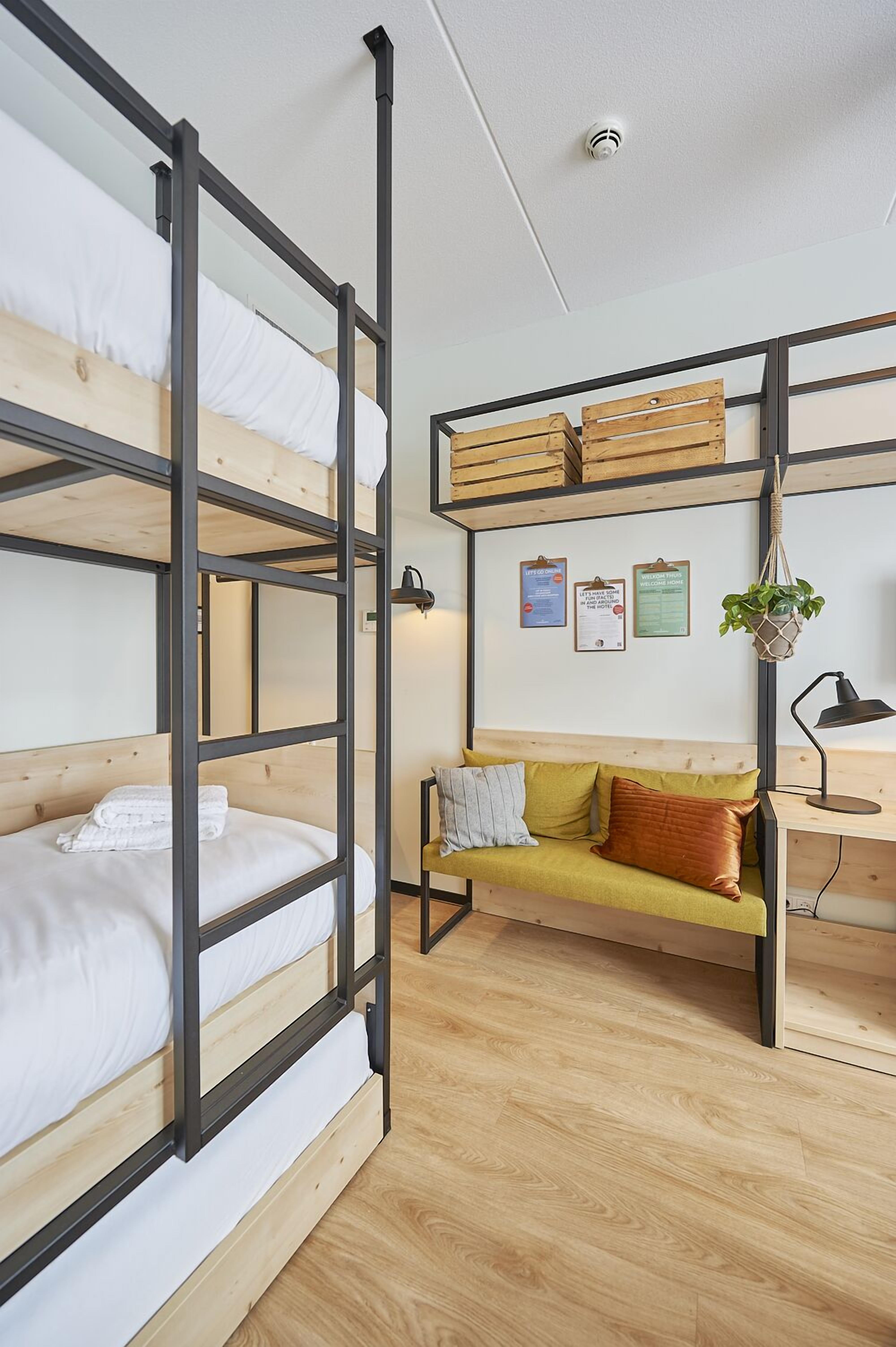 Ein Schlafzimmer mit Etagenbetten, Holzboden, einer Couch und einem Schreibtisch mit hängender Pflanze.